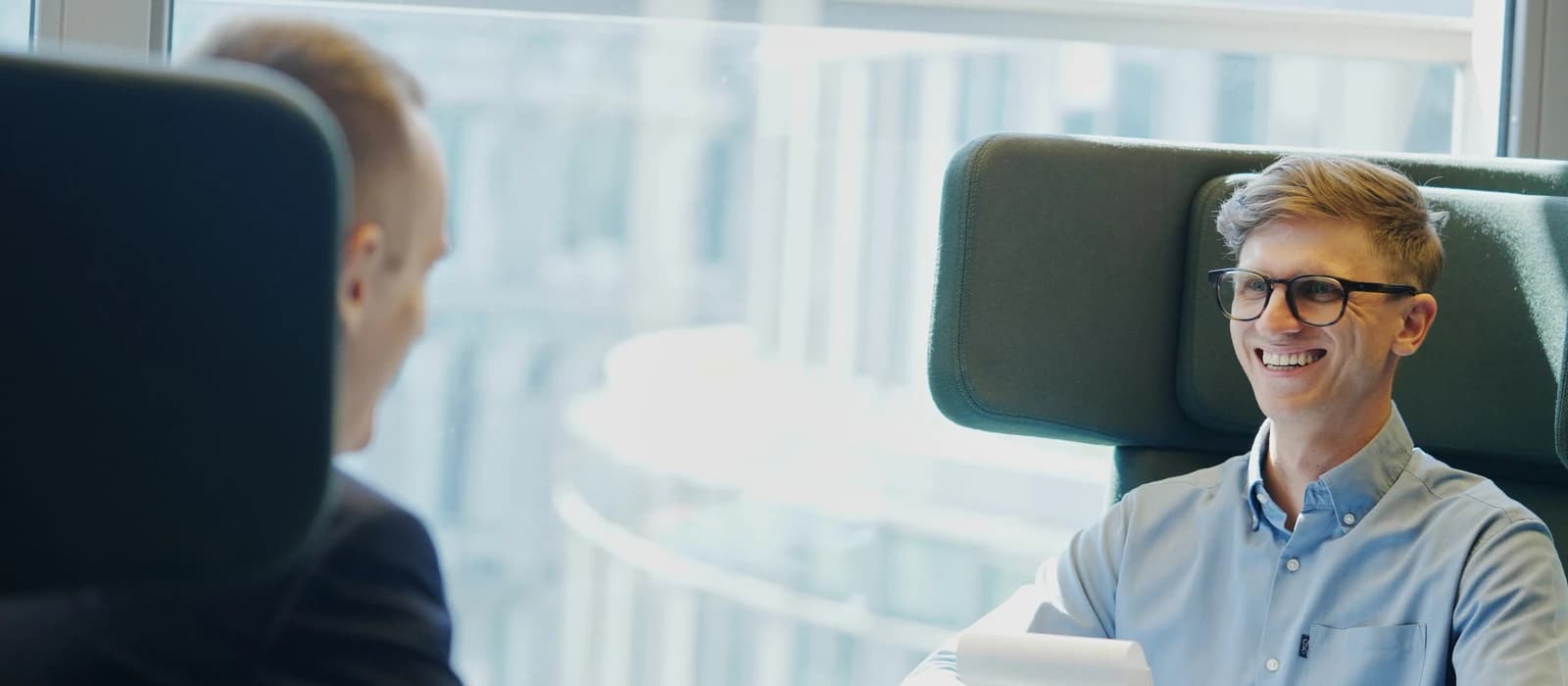Führungskräfte-Coaching: zwei Männer im Gespräch in einem hellen Büro, einer lächelt seinem Gegenüber zu