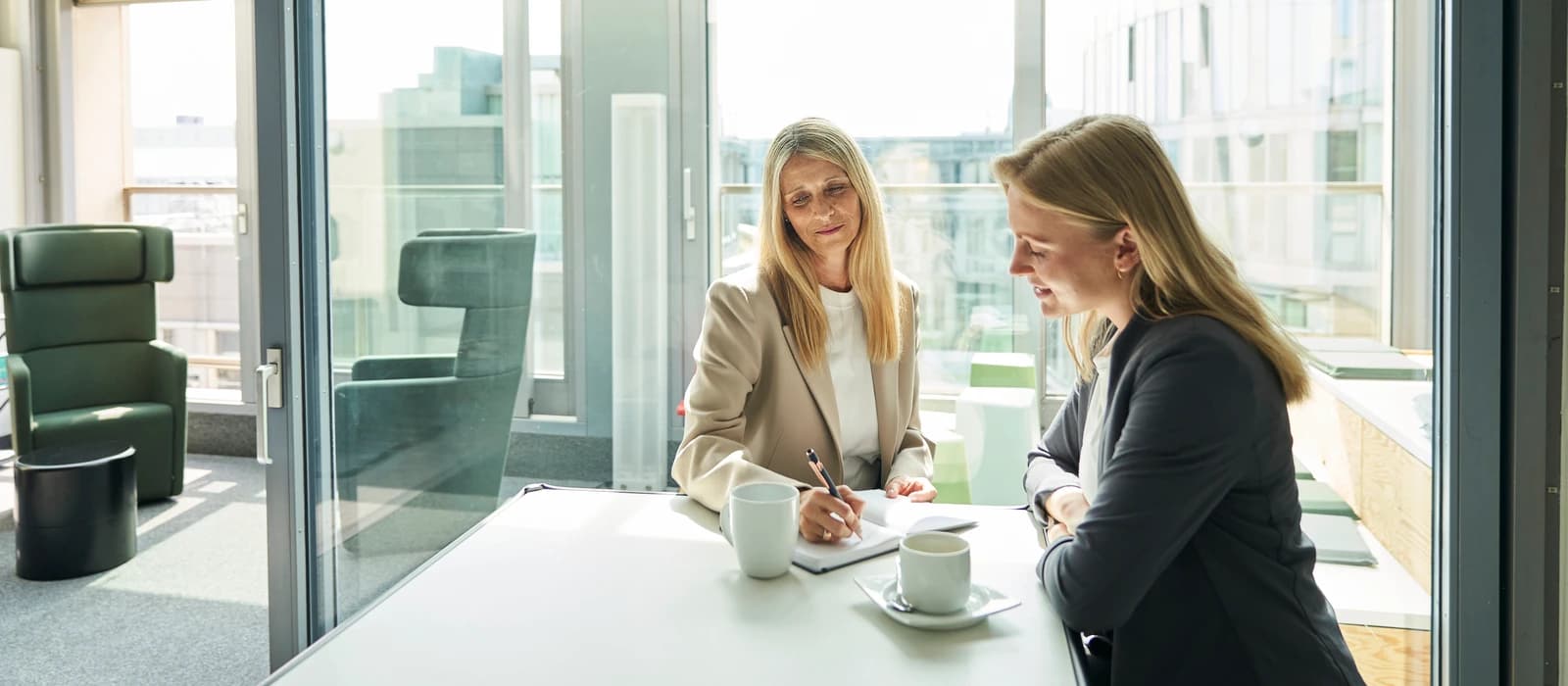 Softwareentwickler besetzen: Beratungsgespräch zwischen zwei Frauen an einem Tisch in einem hellen Büro, eine macht sich Notizen
