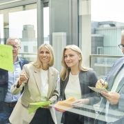 Vier Geschäftspersonen arbeiten gemeinsam an einem Workshop mit bunten Moderationskarten vor einer Glaswand.
